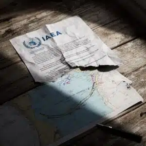 A torn nuclear agreement document with the IAEA logo, sitting on top of a naval map of the Persian Gulf.