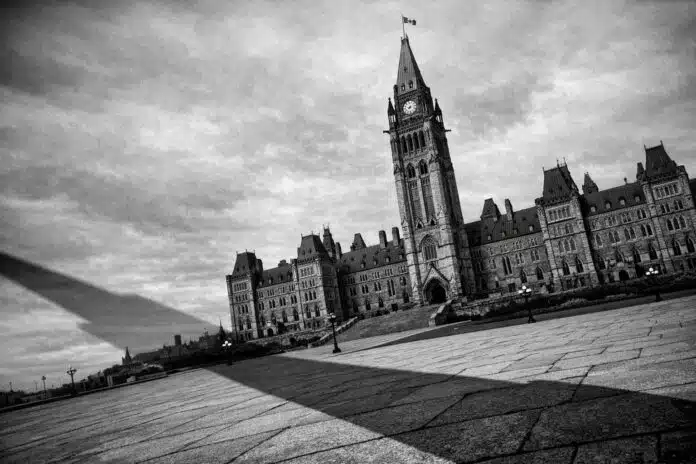 Canada's Democracy: Black and white photo of the Canadian Parliament buildings, slightly tilted, with a long shadow falling across the foreground.