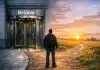 Beyond Reform: The Case for Structural, Transformative Change Structural change: A person standing at a crossroads: one path leads to a polished revolving door labelled "Reform," the other to a rough path leading to a horizon with rising sun.